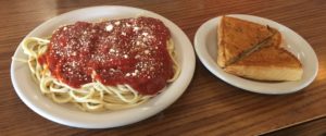 Spaghetti with red sauce and parmesan on a white plate next to a small plate with toast