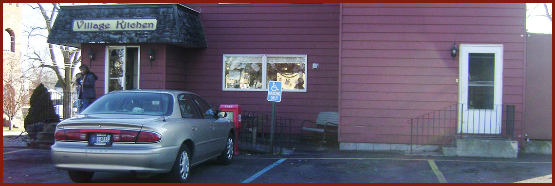 Front of the Village Kitchen in Angola, IN in a red vinyl building with a Ford Taros out front