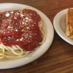 Spaghetti with red sauce and parmesan on a white plate next to a small plate with toast