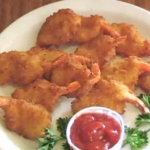Fried shrimp on a place next to a container of ketchup and herbs